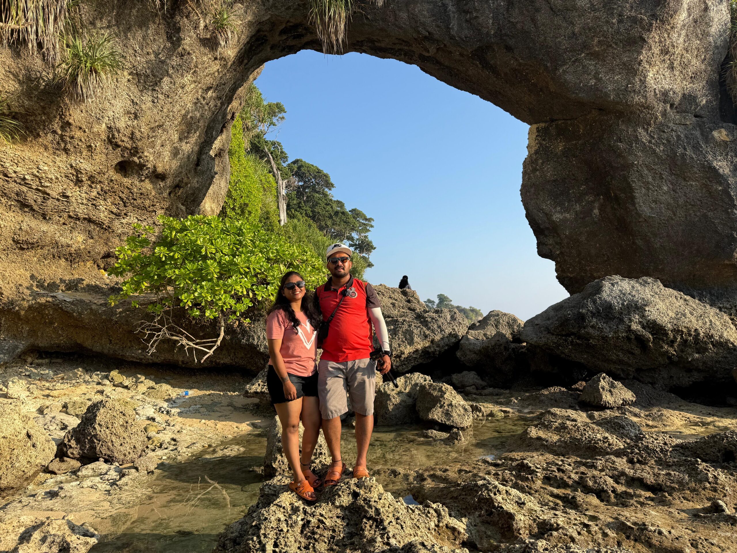 A couple standing in front of the Natural bridge which is a must see attraction in Neil Island
